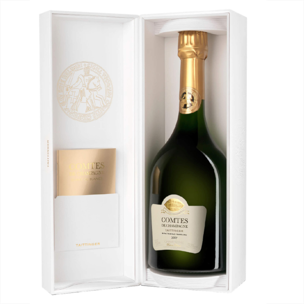 En flaske champagne, pakket i en hvid luksuriøs æske. Etiketten siger: "Comtes de Champagne Taittinger 2007 Blanc de Blancs". Øverst er et gyldent segl præget.